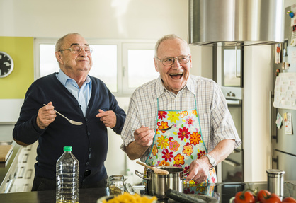 Two happy senior friends cooking in kitchen