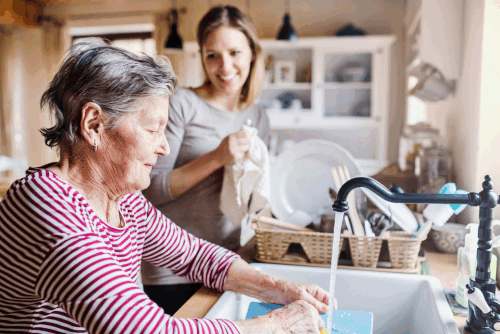 Seniorin macht den Abwasch und wird von einer Helferin unterstützt